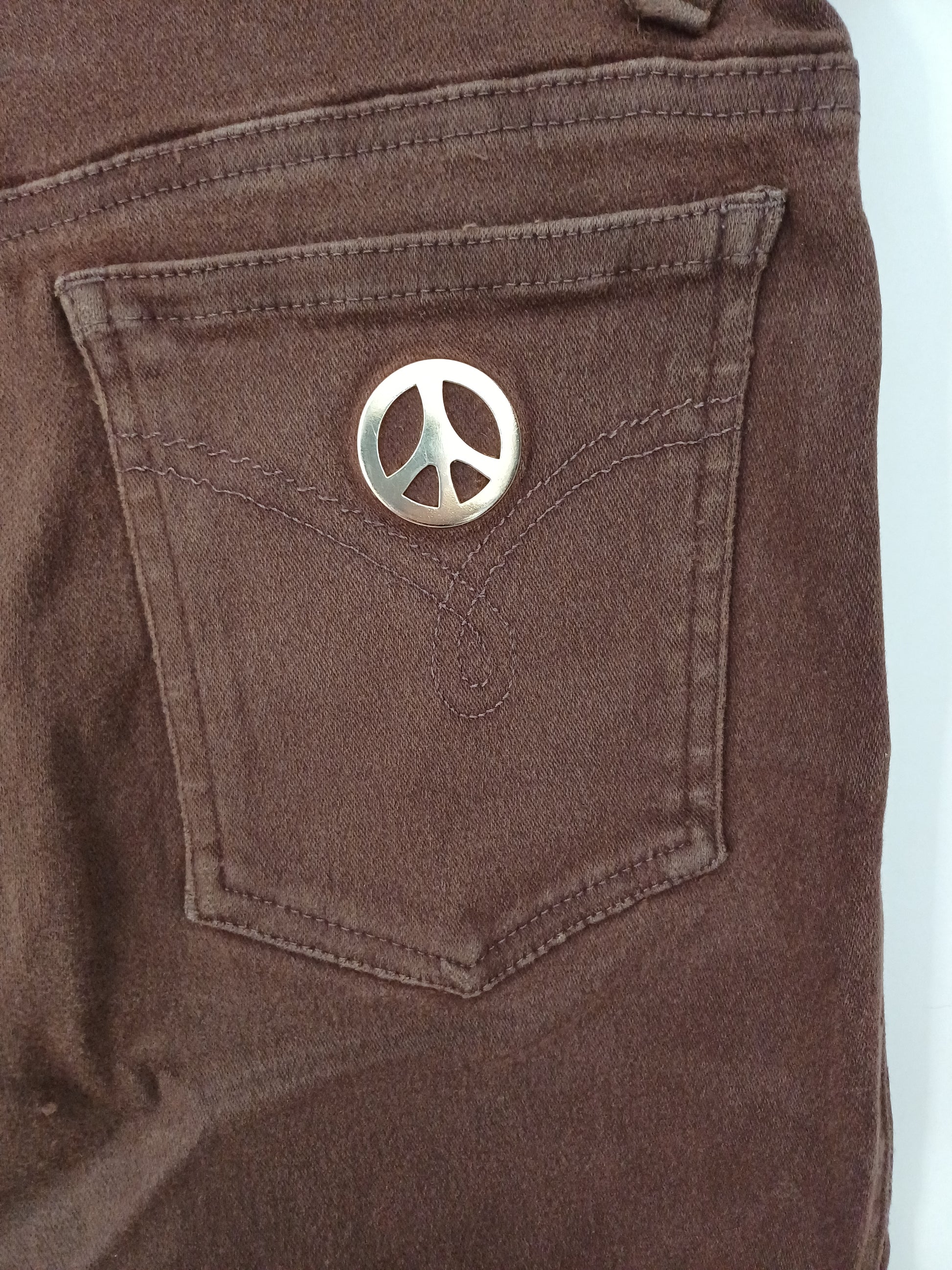 Close-up of a brown fabric pocket with a metallic emblem on a light blue background